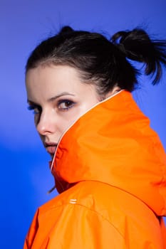 brunette woman in orange jacket, blue background. High quality photo