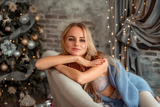 A young blonde woman is sitting on the sofa. The room is decorated with a Christmas tree