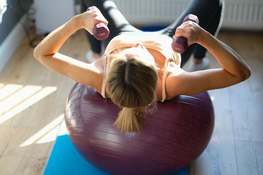 Top view of woman working out with dumbbells on fitness ball at home. Young female doing fitness exercise with dumbbells. Healthy lifestyle concept