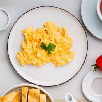 Scrambled eggs, Omelette. Breakfast with pan-fried eggs, cup of tea, tomatoes on white stone marble background. Top view.
