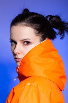 brunette woman in orange jacket, blue background. High quality photo