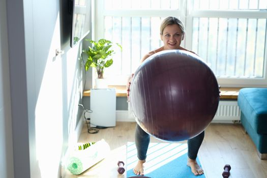 Portrait of sporty smiling woman doing exercises with fitness ball at home. Healthy lifestyle and fitness equipment for sport activity concept