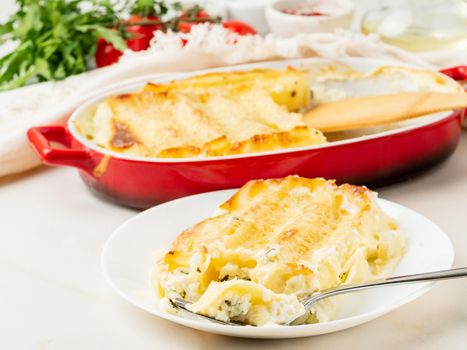 Cannelloni with filling of ricotta and parsley, baked with béchamel sauce, side view, white marble background