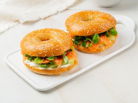 Two sandwiches with salmon, cream cheese, cucumber slices on white marble table