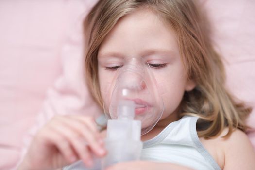 Portrait of sad little girl having inhalation for easing cough. Child in medical oxygen mask lying in bed. Labored breathing, lack of oxygen or inhalation concept