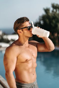 A young man with big muscles drinks a protein shake. High quality photo