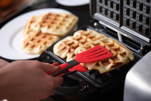 Close-up of waffle iron in kitchen, cooking homemade waffles. Woman preparing yummy breakfast for family