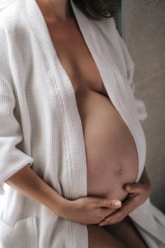 A pregnant woman sits in a white coat, holds her belly with her hands. High quality photo
