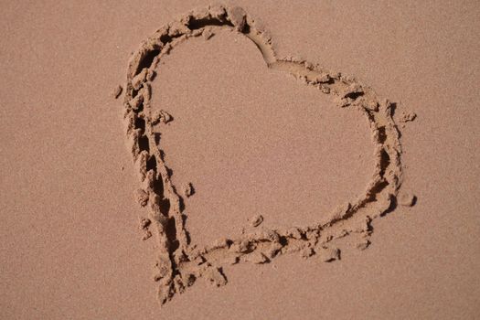 Top view of heart drawn in wet sand, beach background. Love sign on sand. Romantic composition and lovers concept