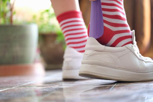 Close-up of person puts shoes white sneakers using shoehorn. Sport or casual shoes. Going for walk concept