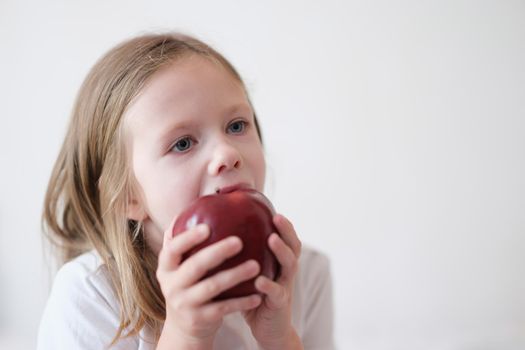 Portrait of little girl eating heartily fresh red apple. Small child holding big apple in hands. Healthy food and vitamins