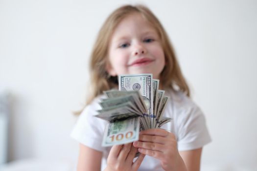 Portrait of little smiling girl counting money, happy childhood. Small cheerful kid holding cash in hands