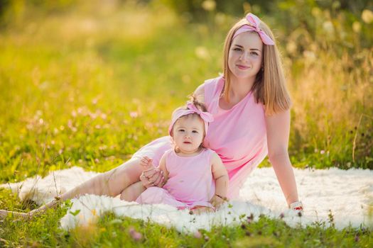 mother and daughter in identical pink dresses are sitting in nature