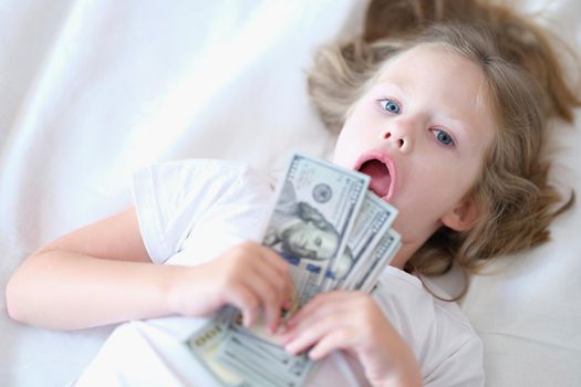 Portrait of small cheerful girl holding cash in hands. Little smiling child counting money, happy childhood.