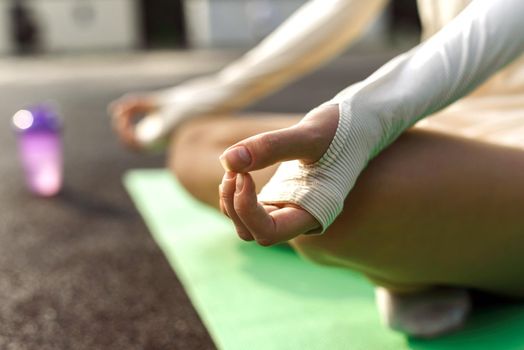 A woman practices yoga and meditates in the stadium in the evening at sunset. Close up of a woman's hands with a zen gesture. Lotus position.