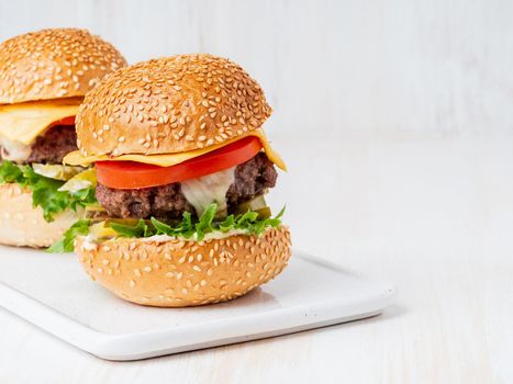Two hamburgers on white board on white background, hot homemade unhealthy fat food, copy space