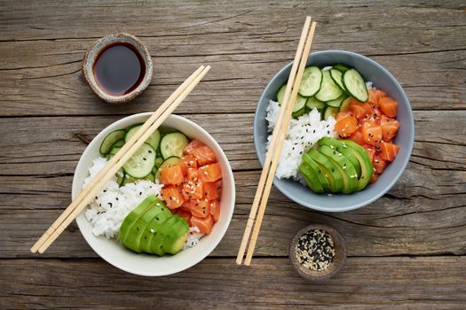 Salmon poke bowl with fresh fish, rice, cucumber, avocado with black and white sesame. Old wooden table. Food concept.