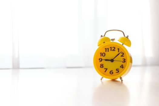 on a white table near the window with white curtains, there is a yellow alarm clock. copy space