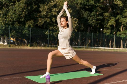 Young beautiful sports model stretches out at the outdoors stadium in the park. A woman goes in for sports and gets in shape