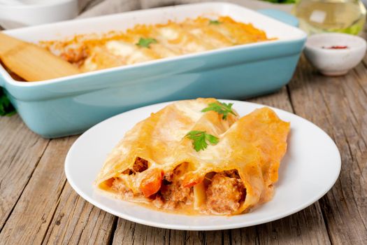 Cannelloni with filling of ground beef, tomatoes, baked with bechamel tomato sauce, side view, old dark wooden background