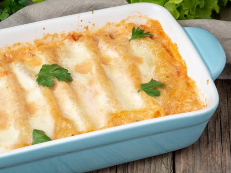 Cannelloni with filling of ground beef, tomatoes, baked with bechamel tomato sauce, side view, old dark wooden background