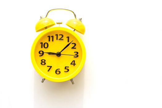 A yellow retro alarm clock with a black dial lies on a white table on the left. top view. copy space