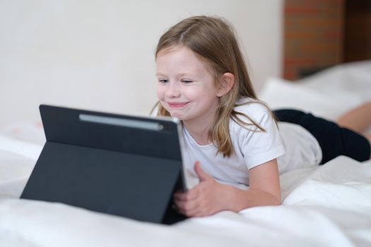 Portrait of smiling cheerful kid having fun with modern tablet. Happy girl having video call with friends or relatives. Happy childhood concept