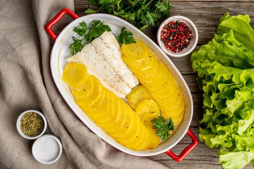 Fish cod baked in oven with potatoes and spice - healthy diet food. Dark wooden brown background, top view.