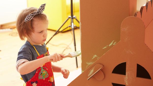 Side view of girl drawing on carton house and having fun at home