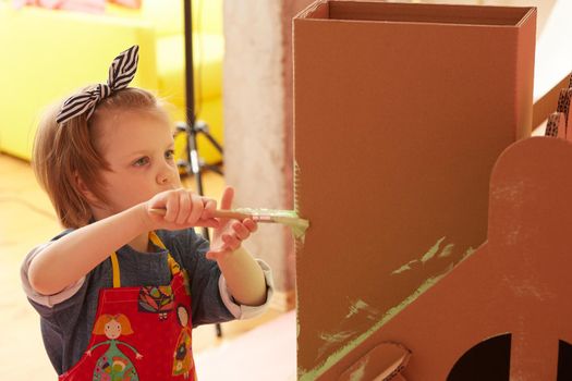 Side view of girl drawing on carton house and having fun at home