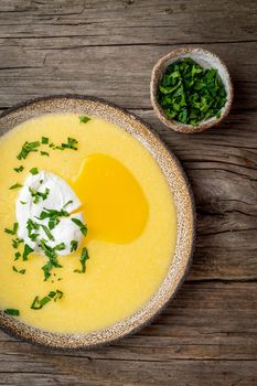 Polenta, porridge with Parmesan cheese and poached egg, vertical on old dark wooden background, top view. traditional Italian cuisine
