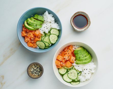 Salmon poke bowl with fresh fish, rice, cucumber, avocado with black and white sesame. White marble table. Food concept.