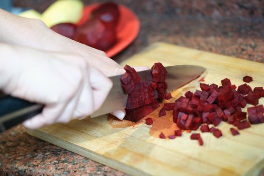 Close-up of woman cutting red beet root, ingredients for dish. Beetroot cube slice. Female preparing dinner. Cooking concept