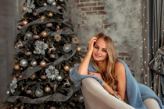A young blonde woman is sitting on the sofa. The room is decorated with a Christmas tree