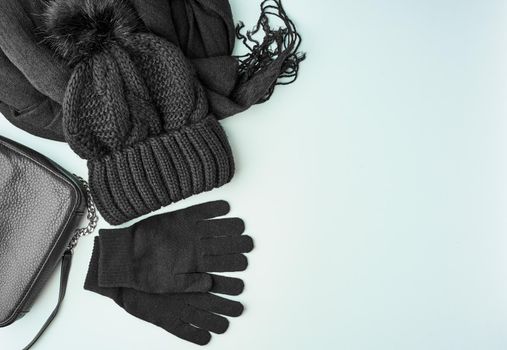Flat lay winter or autumn warm woman accessories - black knitted scarf, hat, bag on bright blue background, copy space.