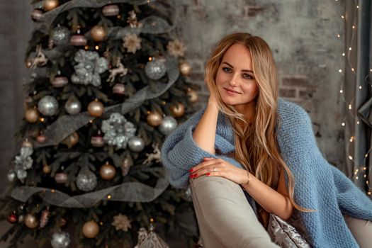 A young blonde woman is sitting on the sofa. The room is decorated with a Christmas tree
