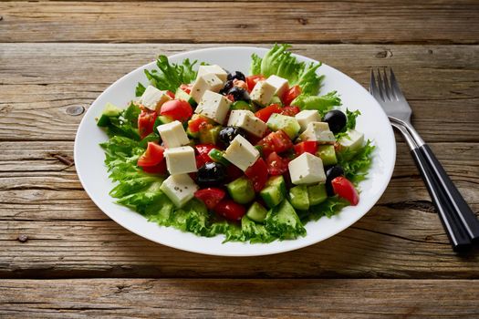 Greek salad on white plate on old rustic wooden table, side view