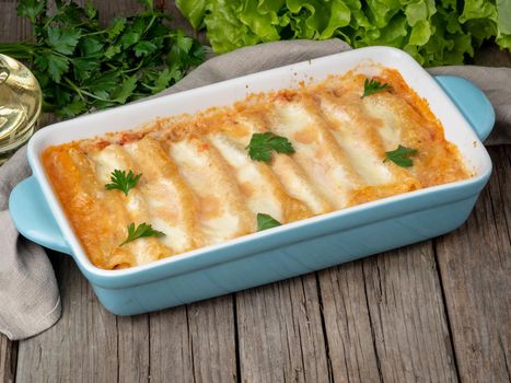 Cannelloni with filling of ground beef, tomatoes, baked with bechamel tomato sauce, side view, old dark wooden background