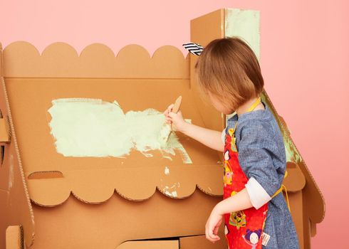 Side view of girl drawing on carton house and having fun at home