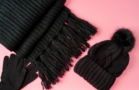 Flat lay winter or autumn warm woman accessories - black knitted scarf, hat, bag on bright pink background, copy space.
