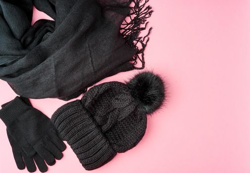 Flat lay winter or autumn warm woman accessories - black knitted scarf, hat on bright pink background, copy space.