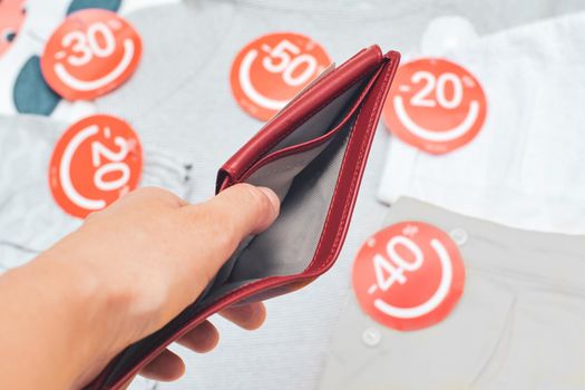 Female hands holding empty red purse background with clothes with discount labels