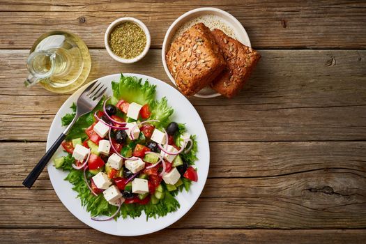 Greek salad on white plate on old rustic wooden table, top view, copy space
