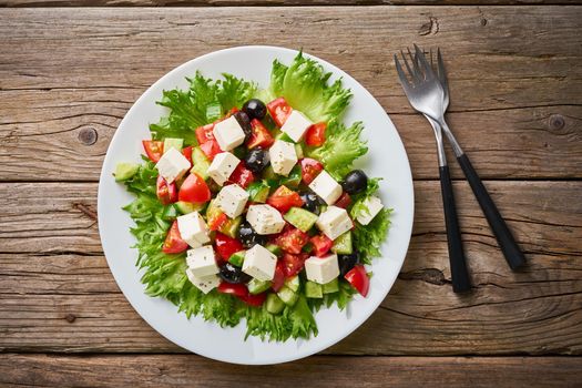 Greek salad on white plate on old rustic wooden table, top view