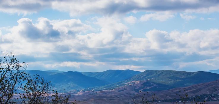 Mountainous terrain on a bright sunny day with a tree in the foreground.