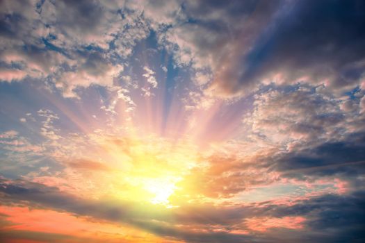 Sun rays look through dark stormy clouds at sunset.