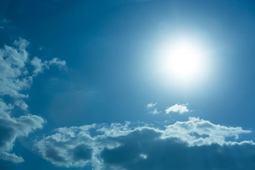 White sunlight rays on blue cloudy sky.