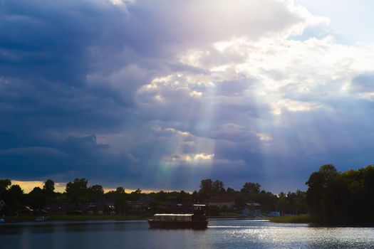Rays of the sun making their way through the clouds over the lake, with houses on the shore.