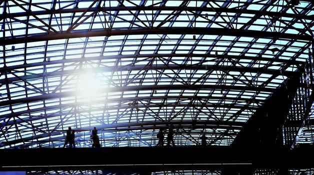 People on a pedestrian walkway with a railing under a glazed metal dome