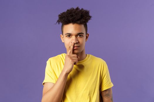 Close-up portrait of funny and unappropriate young hispanic teenage guy picking nose with finger, smiling and looking at camera, standing purple background, have bad habit.